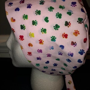 May include: Pink surgical scrub hat with a rainbow paw print pattern.