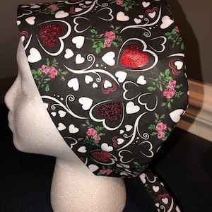 May include: Black scrub hat with a white and red heart pattern. The hat has a tie at the back.