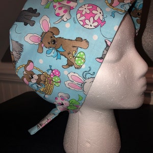 May include: A blue and white patterned surgical scrub hat with a tie. The pattern features cartoon dogs, bunnies, and Easter eggs.