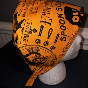 May include: A yellow fabric scrub hat with a black and white print of a spooky Halloween design. The print includes the text "EMBROIDERED SPOOK SILK" and "Duttonholes".