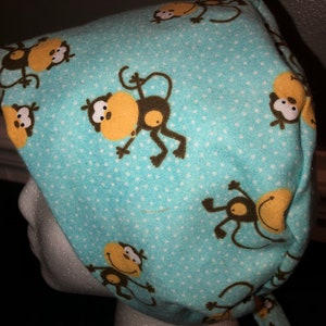 May include: A light blue surgical cap with a white polka dot pattern and a repeating pattern of brown monkeys with yellow faces.