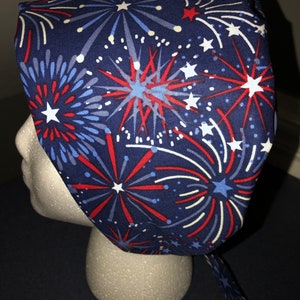 May include: A blue scrub hat with a red, white, and blue firework pattern. The hat has a tie on the back.