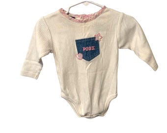 May include: White ribbed long-sleeve baby bodysuit with a denim pocket. The pocket has the word "POOH" embroidered in red, along with a pink heart and star. The neckline is trimmed with a pink floral pattern.