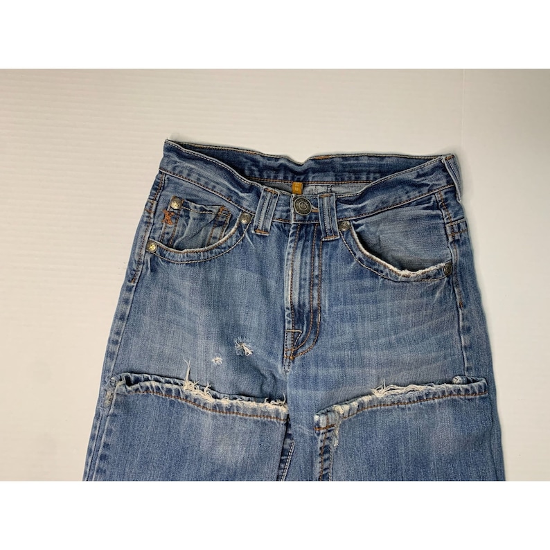 May include: A pair of blue denim jeans with distressed details and a faded wash. The jeans have a button fly and five pockets.