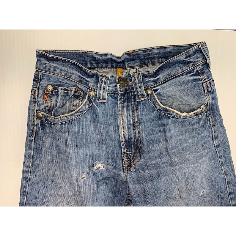 May include: A pair of blue denim jeans with distressed details and a faded look. The jeans have a classic five-pocket style and a button fly.