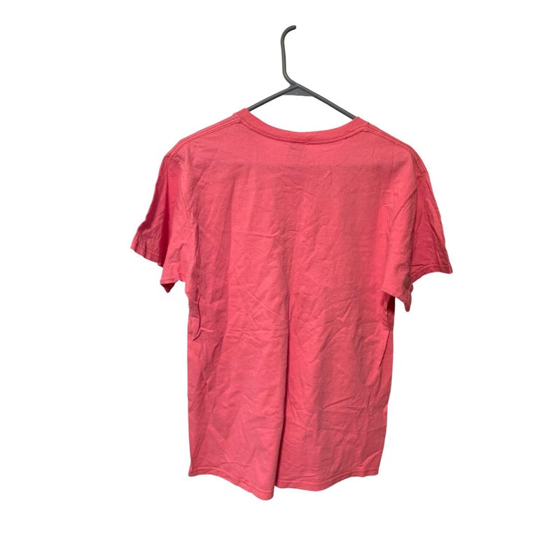 K&ouml;nnte beinhalten: Ein korallenfarbenes T-Shirt h&auml;ngt an einem schwarzen Kleiderb&uuml;gel vor wei&szlig;em Hintergrund. Das kurz&auml;rmelige Shirt besteht aus einem weichen Material und scheint ungetragen zu sein. Die R&uuml;ckseite des Shirts ist sichtbar und zeigt den Ausschnitt und die Textur des Stoffes.