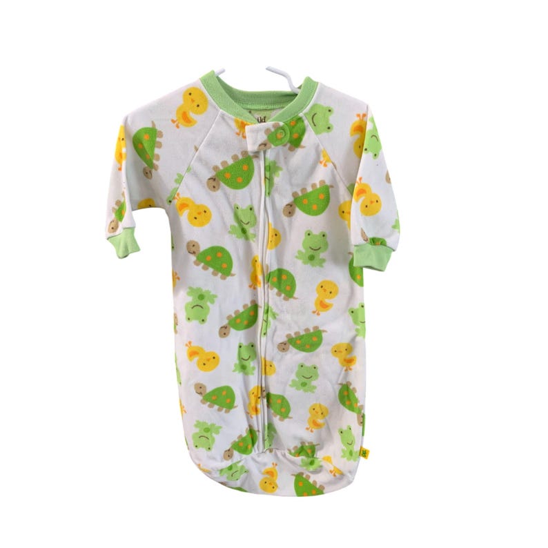 Puede incluir: Pijama de pies blancos con ribete verde y cierre de cremallera. El pijama tiene un patr&oacute;n de tortugas verdes, patos amarillos y ranas verdes.