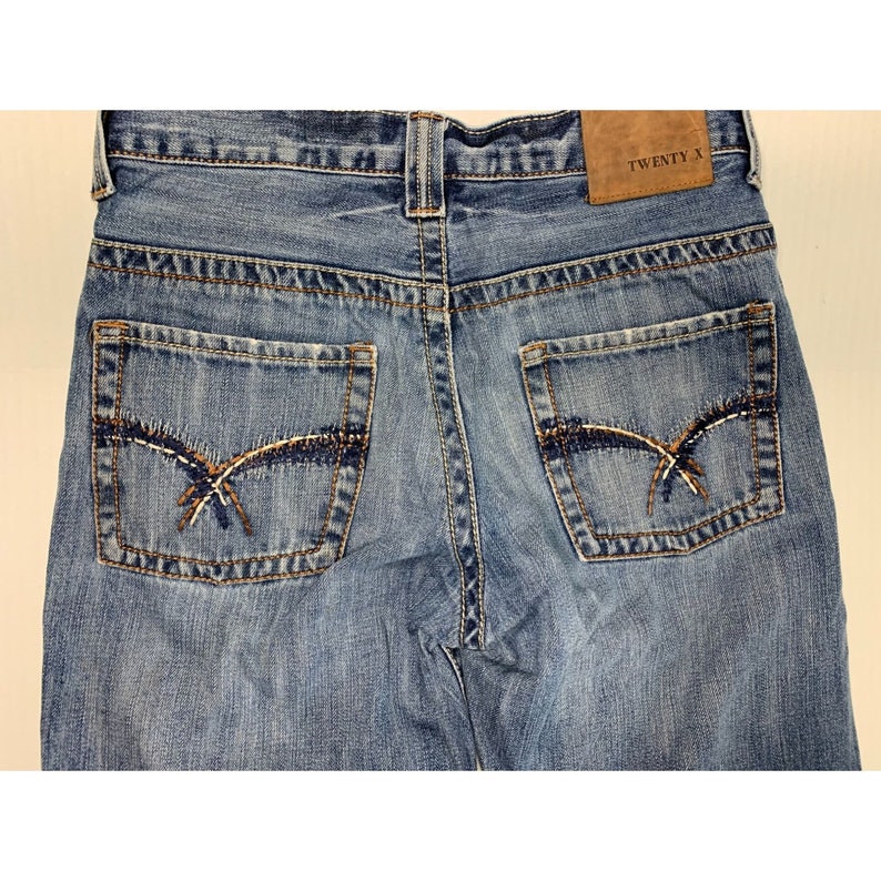 May include: A pair of blue denim jeans with a brown leather patch that says "TWENTY X" on the back. The jeans have two back pockets with decorative stitching.