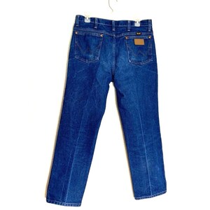 May include: A pair of blue denim jeans with a brown leather patch on the back pocket that says "Wrangler".