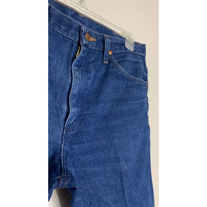 May include: A pair of blue denim jeans with a copper button fly and copper rivets. The jeans have a classic five-pocket style.