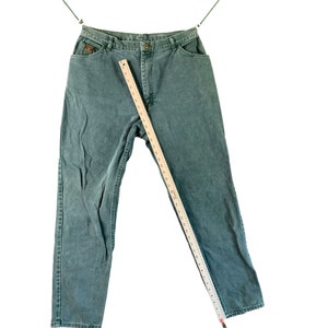 May include: A pair of dark green denim jeans hanging on a clothesline. The jeans have a straight leg and a relaxed fit.