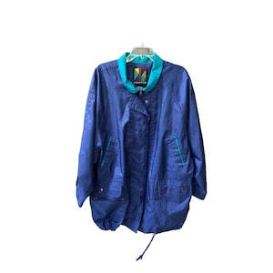 May include: A blue, lightweight jacket with a teal collar and trim. The jacket has a zipper closure and two pockets. The label on the jacket reads "Komito" in a colorful font.