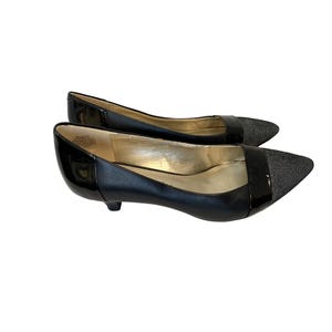 May include: A pair of black low-heeled shoes with a pointed toe. The toe and a band across the top are a textured, light-colored material. The rest of the shoe is black patent leather.