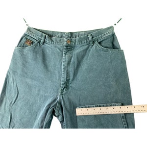 May include: A pair of green denim jeans with a ruler for size reference. The jeans have a straight leg and a classic five-pocket design.