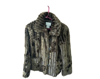 May include: A brown faux fur jacket with a notched collar, button closure, and two front pockets. The jacket is hanging on a pink hanger against a white background. The label reads "Studio 1940".