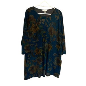 Può includere: Una tunica a maniche lunghe blu turchese con una stampa floreale con fiori gialli, marroni e verdi. La tunica ha un collo rotondo e un orlo posteriore leggermente più lungo.