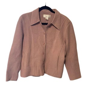 May include: A dusty rose-colored petite jacket with a collared neckline and three buttons. The jacket has a tailored fit with curved seams and three-quarter sleeves. The label reads "PETITE". The jacket is hanging on a black hanger.