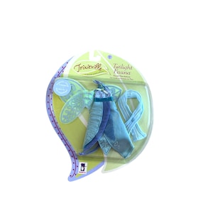 Puede incluir: Un disfraz de hada azul y verde para una muñeca. El disfraz incluye un vestido, alas y una bufanda. El paquete dice "Trixieville" y "Twilight Fauna".