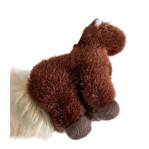 May include: A brown plush horse toy with a shaggy texture. The toy has dark brown hooves and a white patch on its head. The horse is positioned on a white background.
