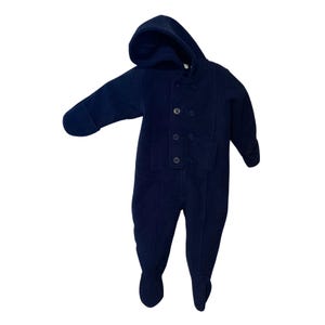 May include: Navy blue baby snowsuit with a hood and button closure. The one-piece garment has long sleeves and attached feet. The snowsuit is made of a soft material.