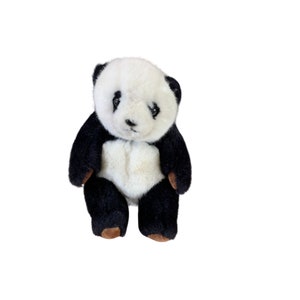 May include: A black and white plush panda bear toy. The panda has a white face with black eyes and a black nose. The panda is sitting up with its paws in front of it.