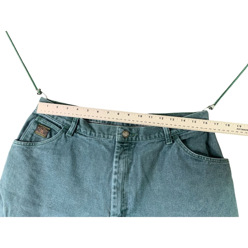 May include: A pair of dark green denim jeans with a wooden ruler measuring the waist at 16 inches.