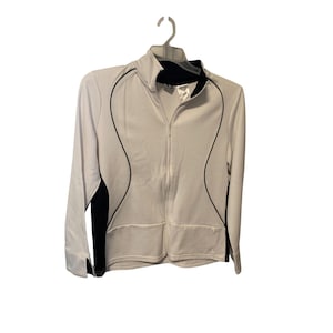 May include: White zip-up jacket with black detailing. The jacket has a high collar, long sleeves, and a full-length zip. Black trim outlines the front and back panels. The jacket is hanging on a white hanger.