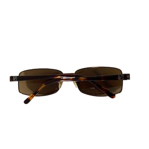 May include: Brown rectangular sunglasses with a tortoiseshell pattern on the arms. The lenses are a solid brown color. The frame has a gold-colored metal rim and a small square logo on the temples.