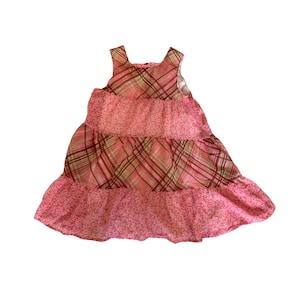 May include: A pink and brown plaid sleeveless dress with a tiered skirt. The dress has a floral print on the bottom tier.