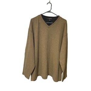 May include: A long-sleeved, olive green V-neck shirt hanging on a black hanger. The shirt has a darker gray undershirt visible at the neckline. The fabric appears to be a soft knit material.
