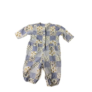 Puede incluir: Un mono de bebé de patchwork blanco y azul con cierre de botón. El mono tiene un estampado floral y geométrico.