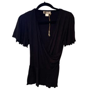 May include: A black wrap-style top with short, ruffled sleeves. The top has a V-neck and a gathered design at the waist. It hangs on a black hanger. A tag is attached to the garment.