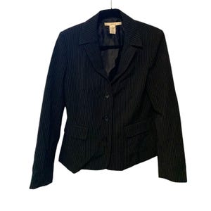 May include: Black pinstripe blazer with a notched collar, three-button closure, and two front pockets. The blazer is hanging on a black hanger. The jacket is size 4.