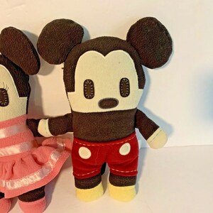 Pu&ograve; includere: Un paio di bambole di peluche di Topolino e Topolina. Topolino indossa pantaloncini rossi con pois bianchi e Topolina indossa un vestito rosa con strisce bianche.