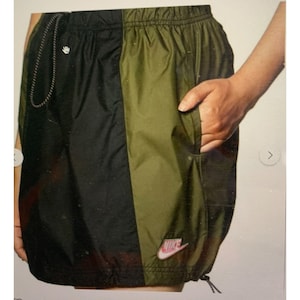 May include: Black and green nylon shorts with a pink Nike logo on the right side. The shorts have a drawstring waist and a side pocket.