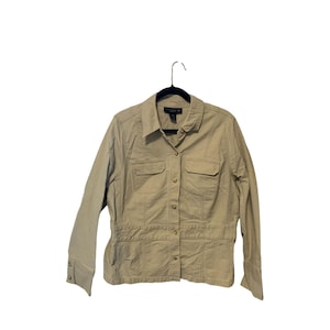 May include: A tan button-down jacket with two chest pockets and two lower pockets. The jacket has long sleeves with buttoned cuffs and a collared neckline. The garment is hanging on a black hanger against a white background.