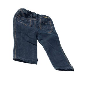 May include: Dark blue denim pants with an elastic waistband and two back pockets. The pants have light brown stitching and a small label on the back pocket. The pants are designed for children.