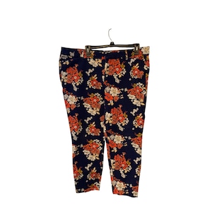 Può includere: Pantaloni blu navy con stampa floreale. I pantaloni presentano un vivace motivo di fiori arancioni e bianchi. I pantaloni sono appesi a una gruccia nera.