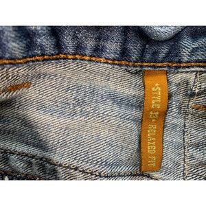May include: Close-up of a blue denim jean with a brown tag that reads "Style 334 Relaxed Fit".