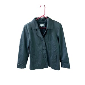 May include: A dark gray blazer with a notched collar, three buttons, and two front pockets. The jacket is hanging on a pink hanger against a white background. The blazer has a classic, tailored design.