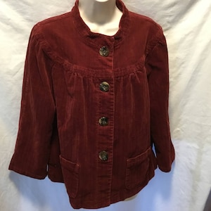 Puede incluir: Una chaqueta de pana color burdeos con cierre de botones y dos bolsillos. La chaqueta tiene un aspecto ligeramente fruncido en la cintura.
