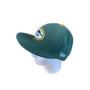 Puede incluir: Gorra de béisbol verde y amarilla con un logotipo "G" blanco en la parte delantera y un logotipo "New Era" blanco en el lateral.