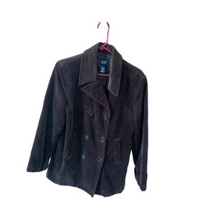 Könnte beinhalten: Eine braune Cordjacke mit doppeltem Knopverschluss und schwarzen Knöpfen. Die Jacke hat einen Kragen und zwei Taschen. Das Etikett auf der Jacke lautet "GAP".