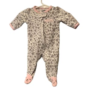 May include: A baby's footed sleeper with a heart pattern in gray and white. The sleeper has a pink trim around the neck, cuffs, and feet. The feet have a bear face design. The zipper runs down the front. The tag reads "Happy & Cozy".