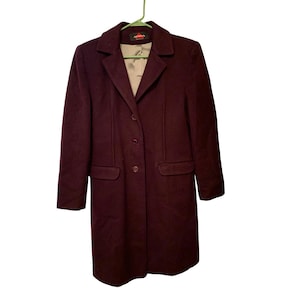 May include: A burgundy wool coat with a classic design. The coat features a notched collar, three buttons, and two front pockets. The coat is hanging on a green hanger.