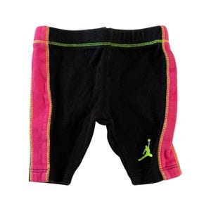 Puede incluir: Leggings negros con ribetes rosa y verde. Los leggings tienen un pequeño logotipo Jumpman verde en la pierna derecha.