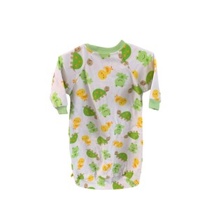 Puede incluir: Un pijama blanco de manga larga con ribete verde y un patr&oacute;n de tortugas verdes, pollitos amarillos y ranas verdes.