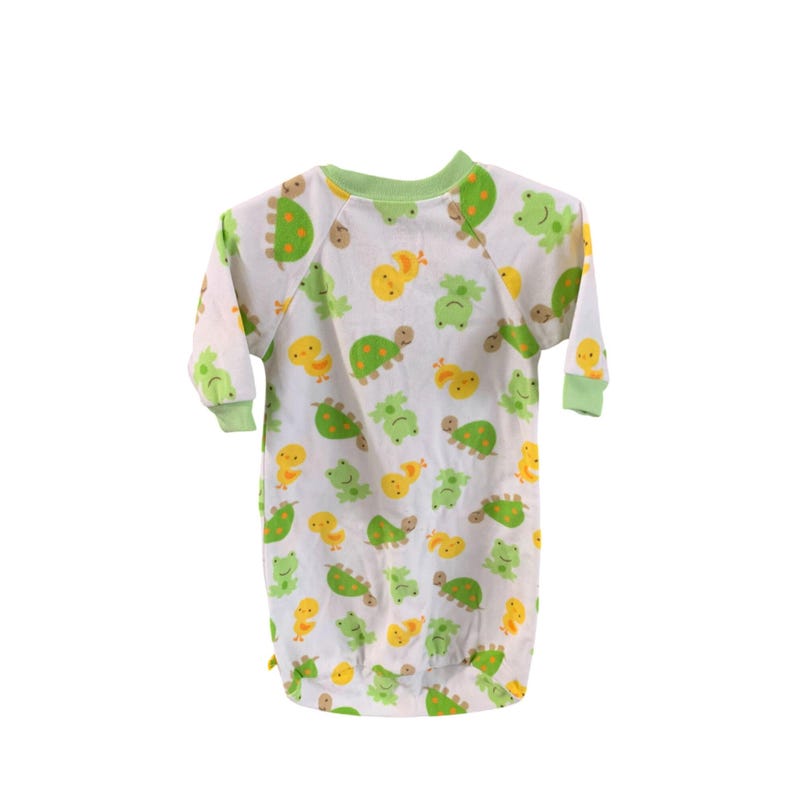 Puede incluir: Un pijama blanco de manga larga con ribete verde y un patr&oacute;n de tortugas verdes, pollitos amarillos y ranas verdes.