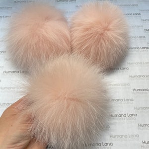 May include: Three fluffy pink faux fur pom poms. The pom poms are soft and round.