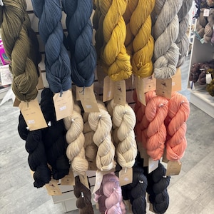 May include: A wall display of yarn skeins in various colors, including black, brown, beige, pink, red, yellow, blue, and gray. The yarn is arranged in rows and is labeled with the word "YARN" at the top.